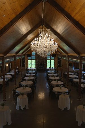 Rustic wooden reception venue with chandelier and round tables arranged for wedding dinner.