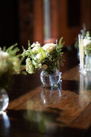 Delicate white and green floral centerpiece arrangement in a glass vase on wooden table.