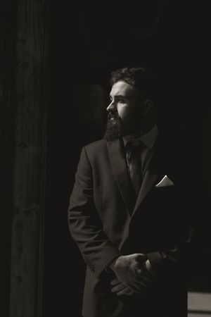 Black and white portrait of suited man with beard in dramatic side lighting.
