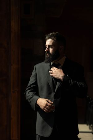 Bearded man in formal attire adjusts his suit jacket in dramatic lighting.