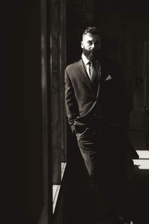 Artistic black and white portrait of suited man standing in contrasting light and shadow.