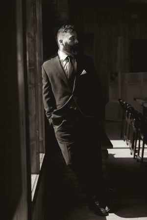 Dramatic black and white photo of person in formal attire standing in shadows.