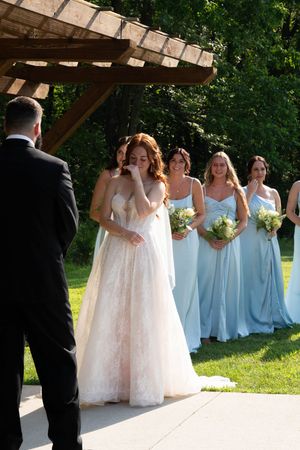 Wedding party in light blue bridesmaid dresses and white gown standing under wooden pergola.