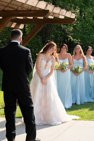 Bride in white gown with bridesmaids in light blue dresses during outdoor ceremony.