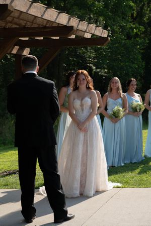 Bridal party lined up under wooden pergola during outdoor wedding ceremony.