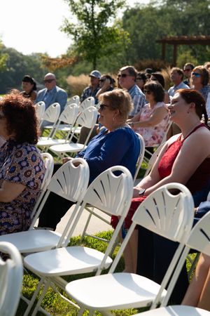 Row of white folding chairs with wedding guests seated outdoors.