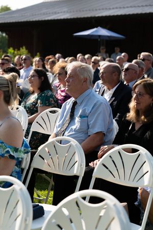 Wedding guests seated in white fan-back chairs during outdoor ceremony.
