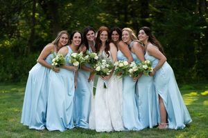 Wedding party in blue and white dresses pose together on grass.