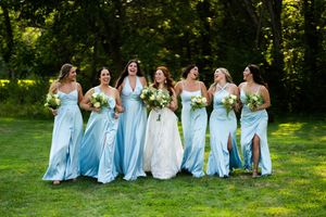 Bridal party in light blue dresses poses on sunny lawn.