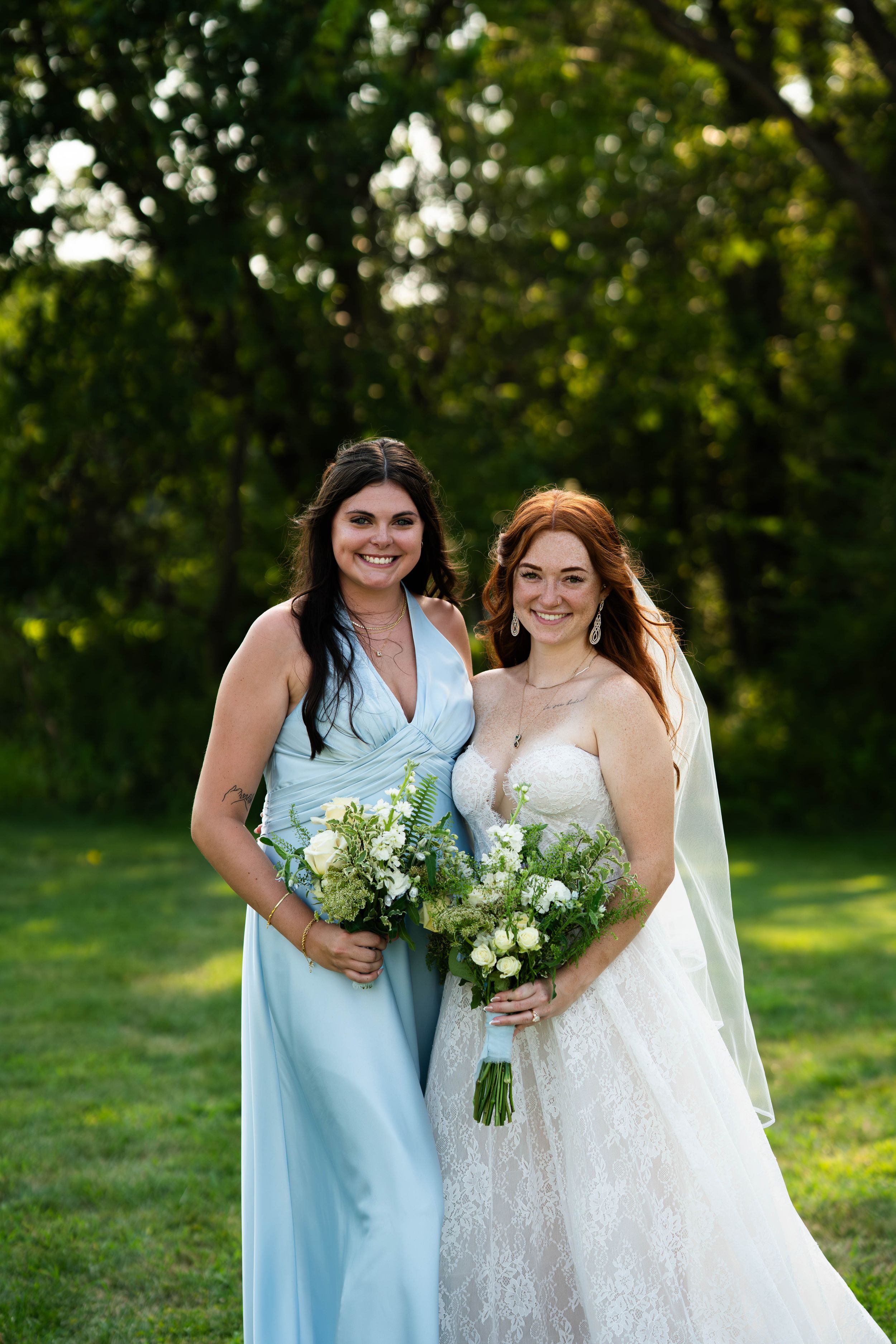 Wedding party members in pale blue dresses gather for outdoor photos with bouquets.
