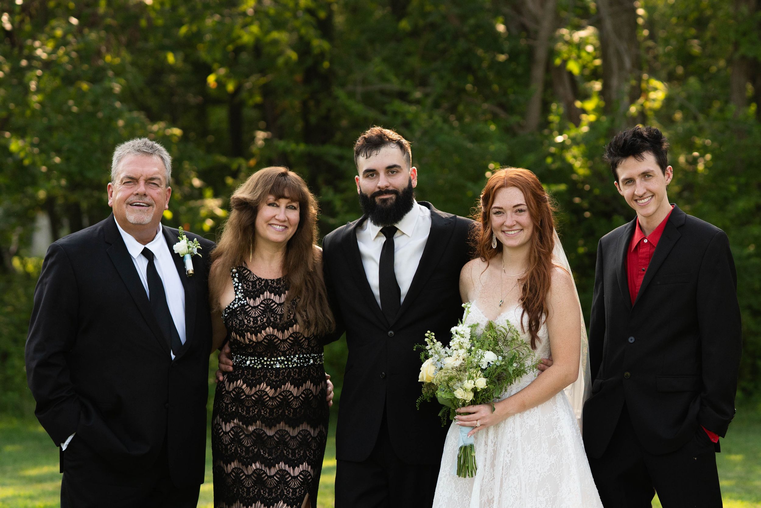 Wedding group photo session in a park with bridesmaids in light blue dresses and groomsmen in black suits.