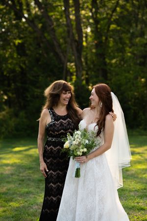 Two people in formal attire share a joyful moment outdoors while holding white flower bouquet.