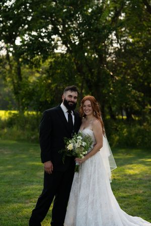 A romantic wedding couple poses together in a sunlit garden setting.