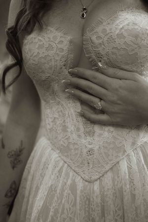 Close-up detail of white lace wedding dress bodice with engagement ring and delicate hand placement.