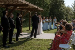 Outdoor wedding ceremony with guests seated in rows along a tree-lined path.
