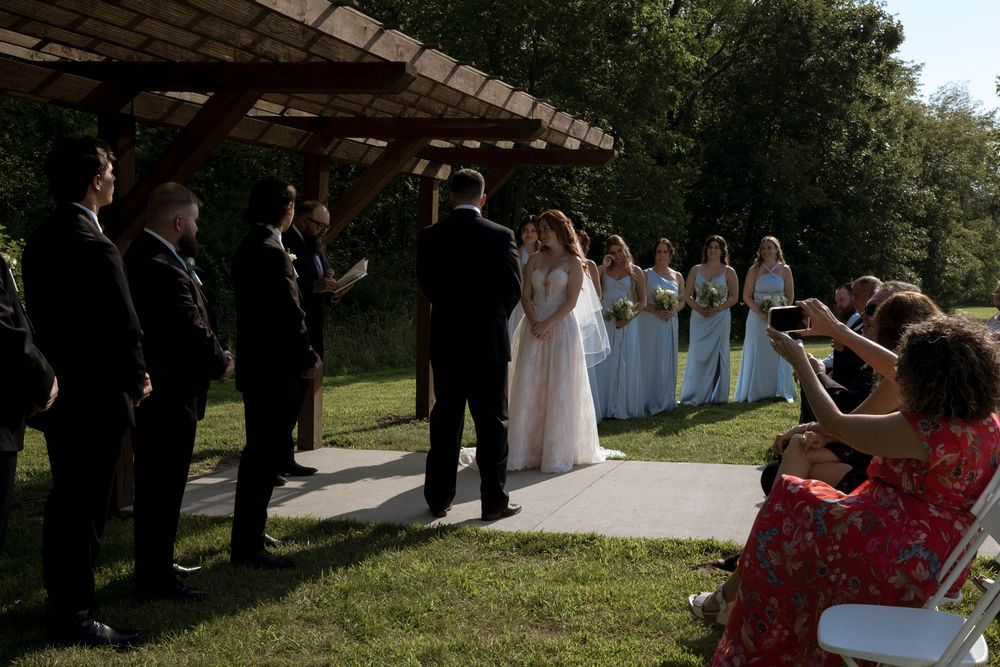Guests line both sides of a covered walkway during an outdoor wedding ceremony.