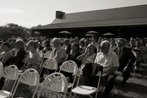 Wedding guests seated in white chairs under a covered outdoor venue.