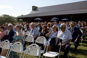 Wedding guests seated in white chairs on a lawn during an outdoor ceremony.