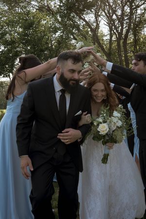 Wedding party celebrating with arms raised in joyful poses outdoors.