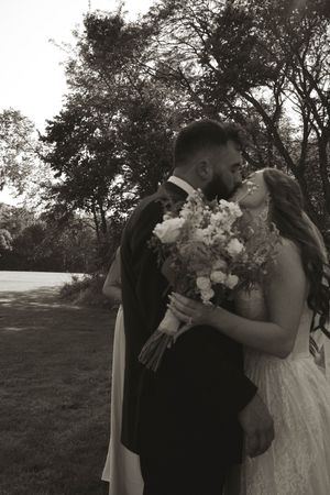 Couple embracing during outdoor wedding photoshoot with white floral bouquet.