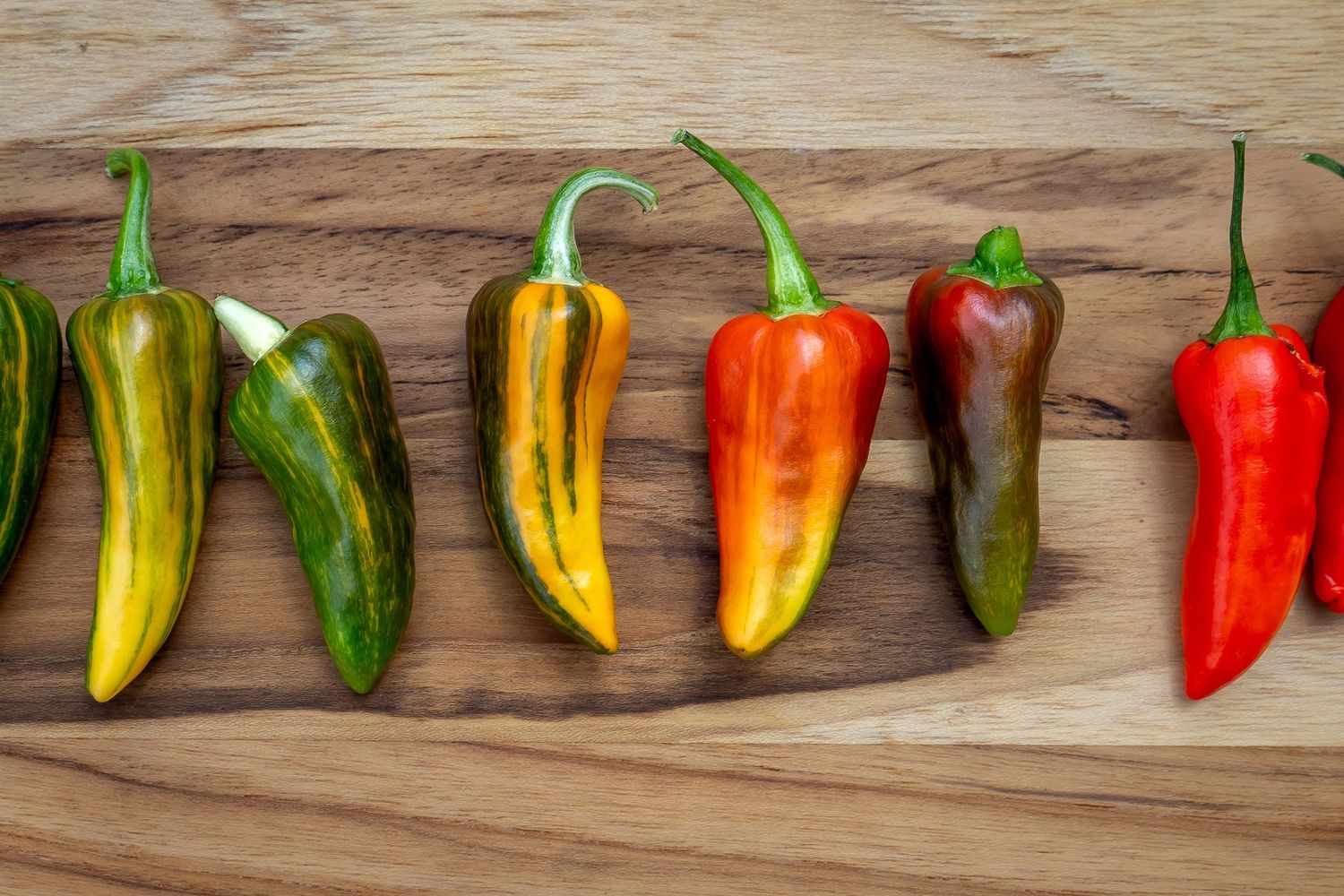 Vibrant chili peppers in various colors and sizes laid out on wooden background.