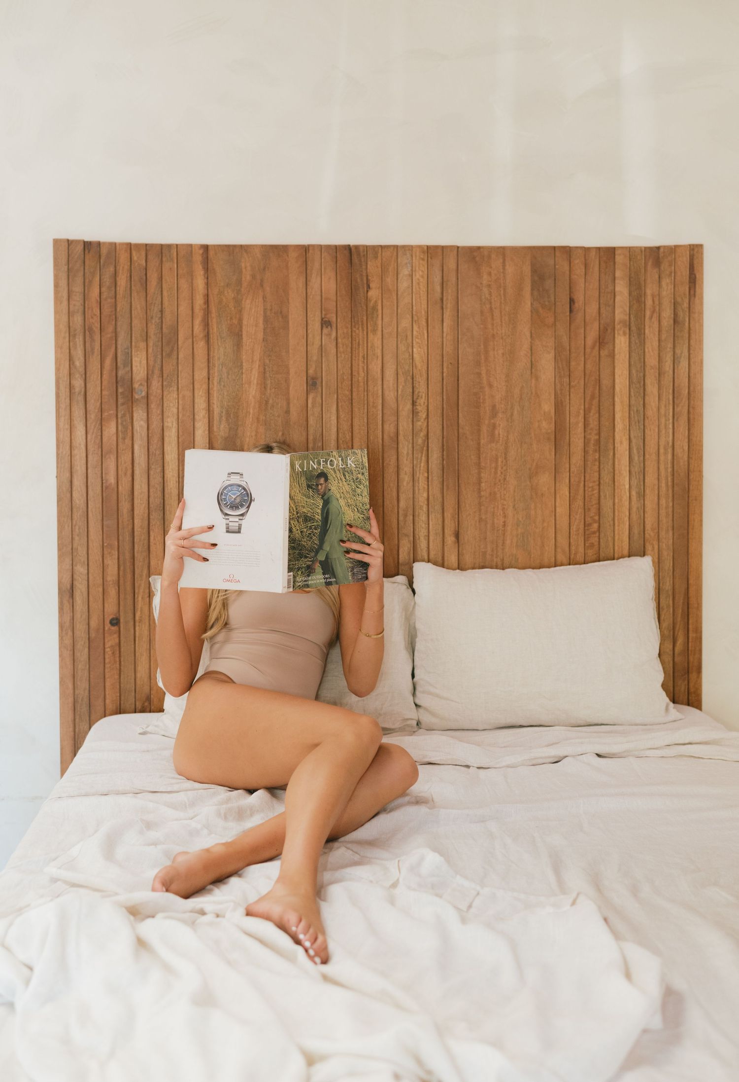A relaxing morning scene with someone reading in bed against a wooden headboard, shot by a nyc branding photographer.