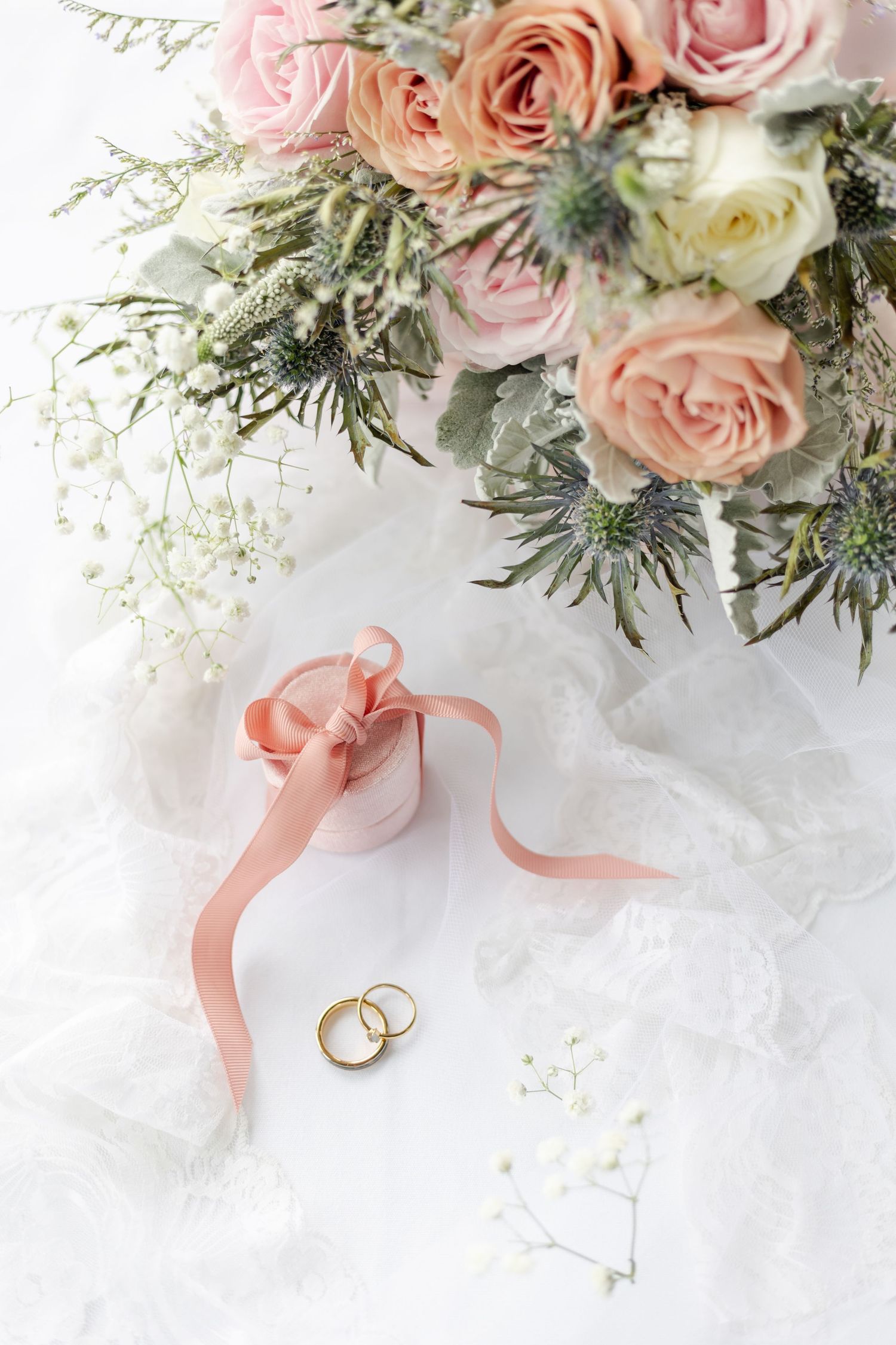 Faded pastel pink hues of floral displays with blush coloured ring box and golden wedding rings