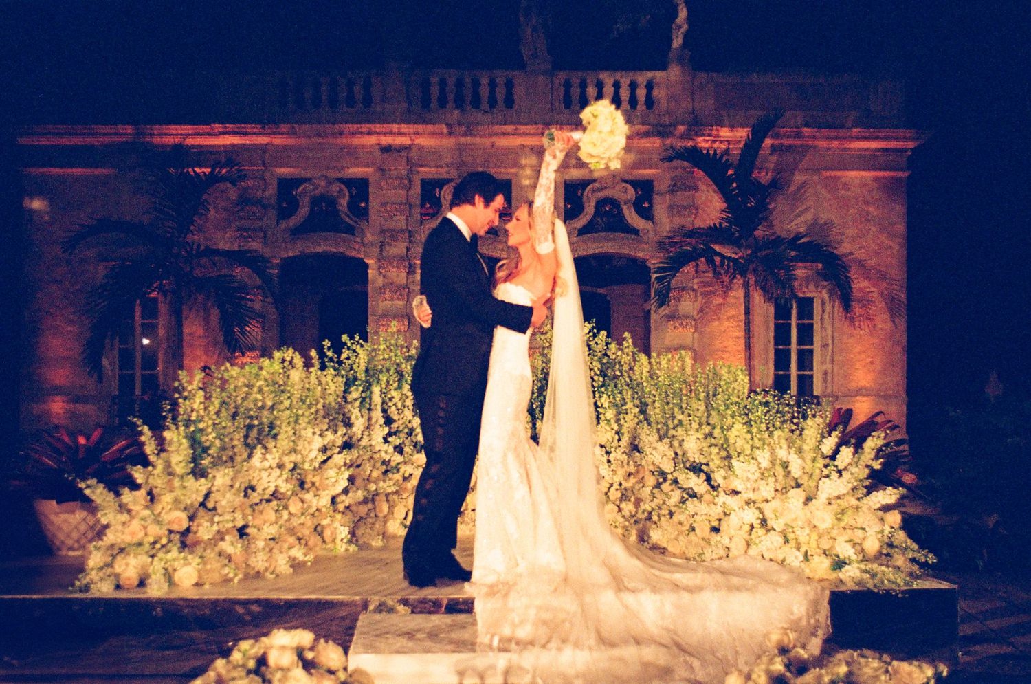 Wedding couple shares romantic dance at night surrounded by glowing lights and floral arrangements at elegant venue.