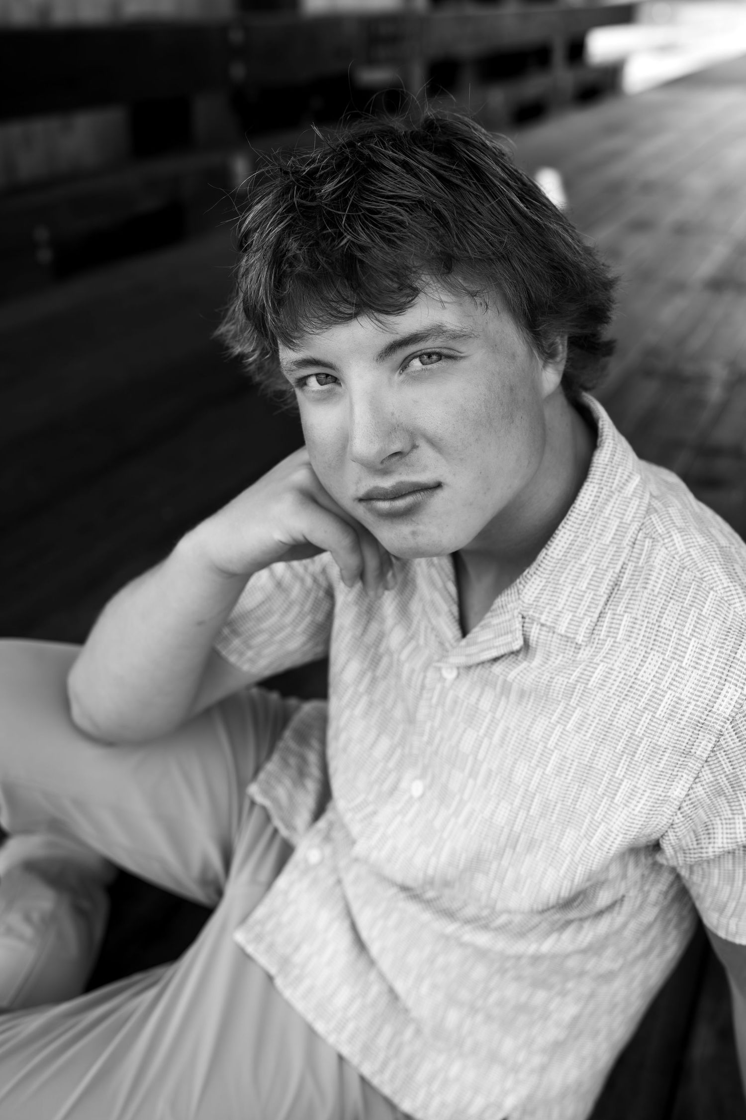 Black and white portrait against white background showing relaxed casual pose in button-down shirt.