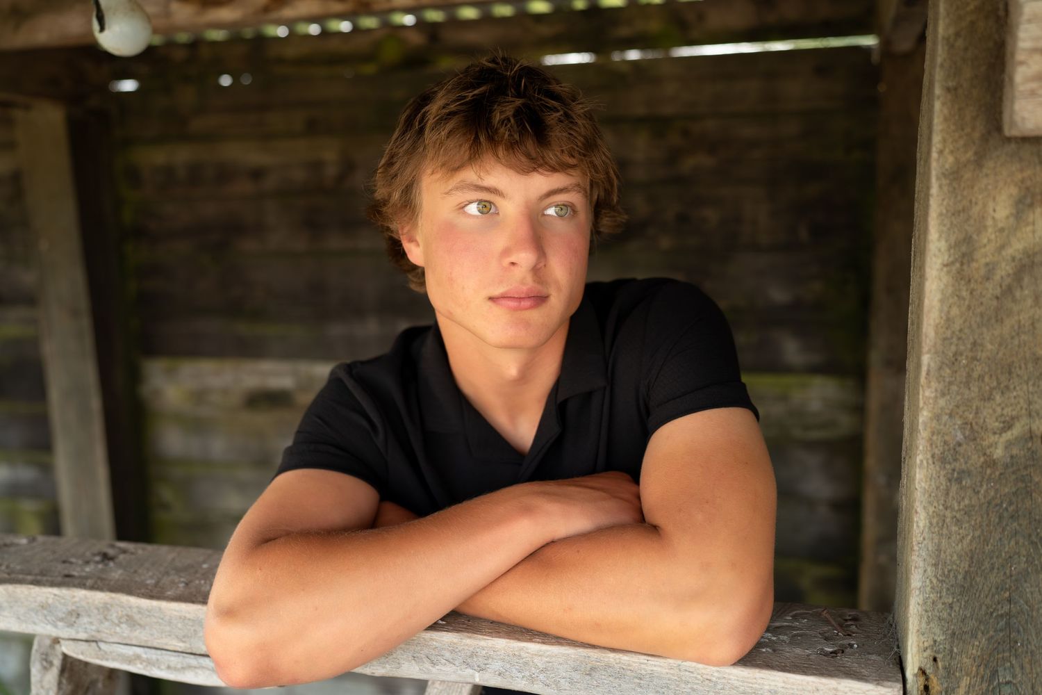 A person in a black t-shirt leans against a wooden railing in a rustic setting with warm lighting.