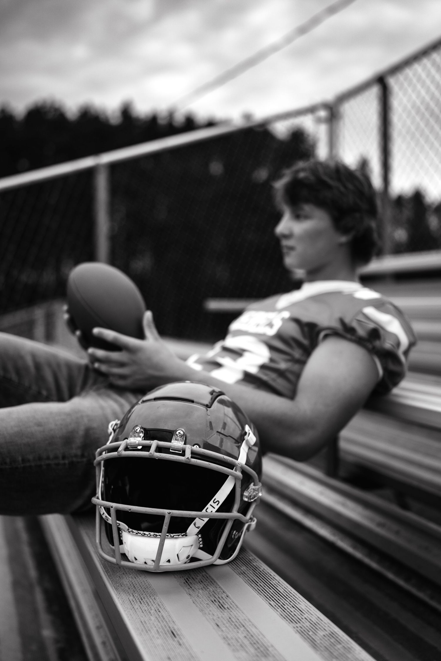 A football player relaxes on bleachers with a helmet and football during a black and white photoshoot.