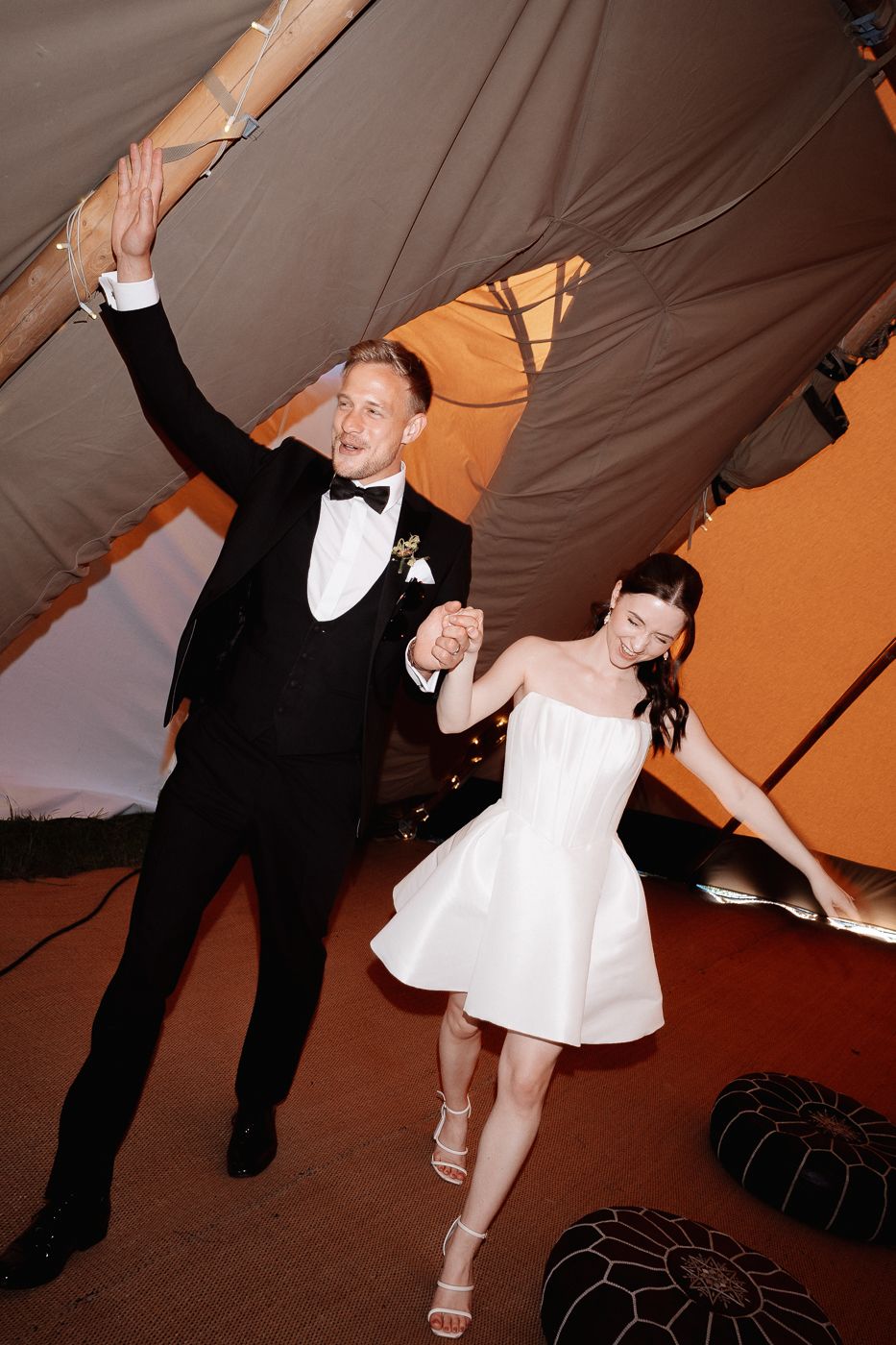 Four sequential action shots show a couple dancing playfully at a wedding reception under a tent with a tan canopy.