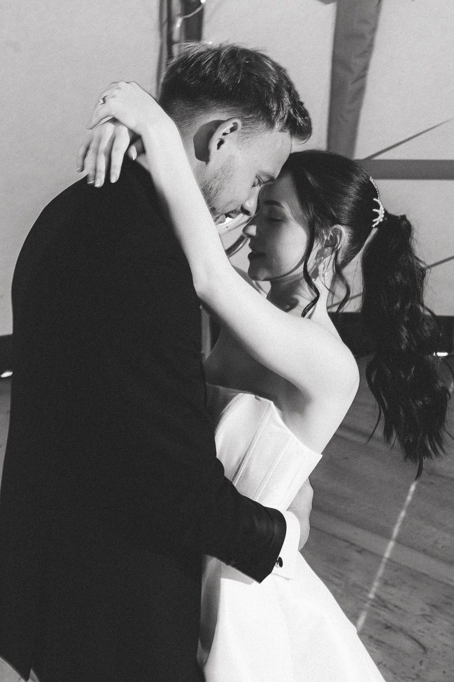 A romantic black and white photograph showing a couple in an intimate dance embrace during their wedding celebration.