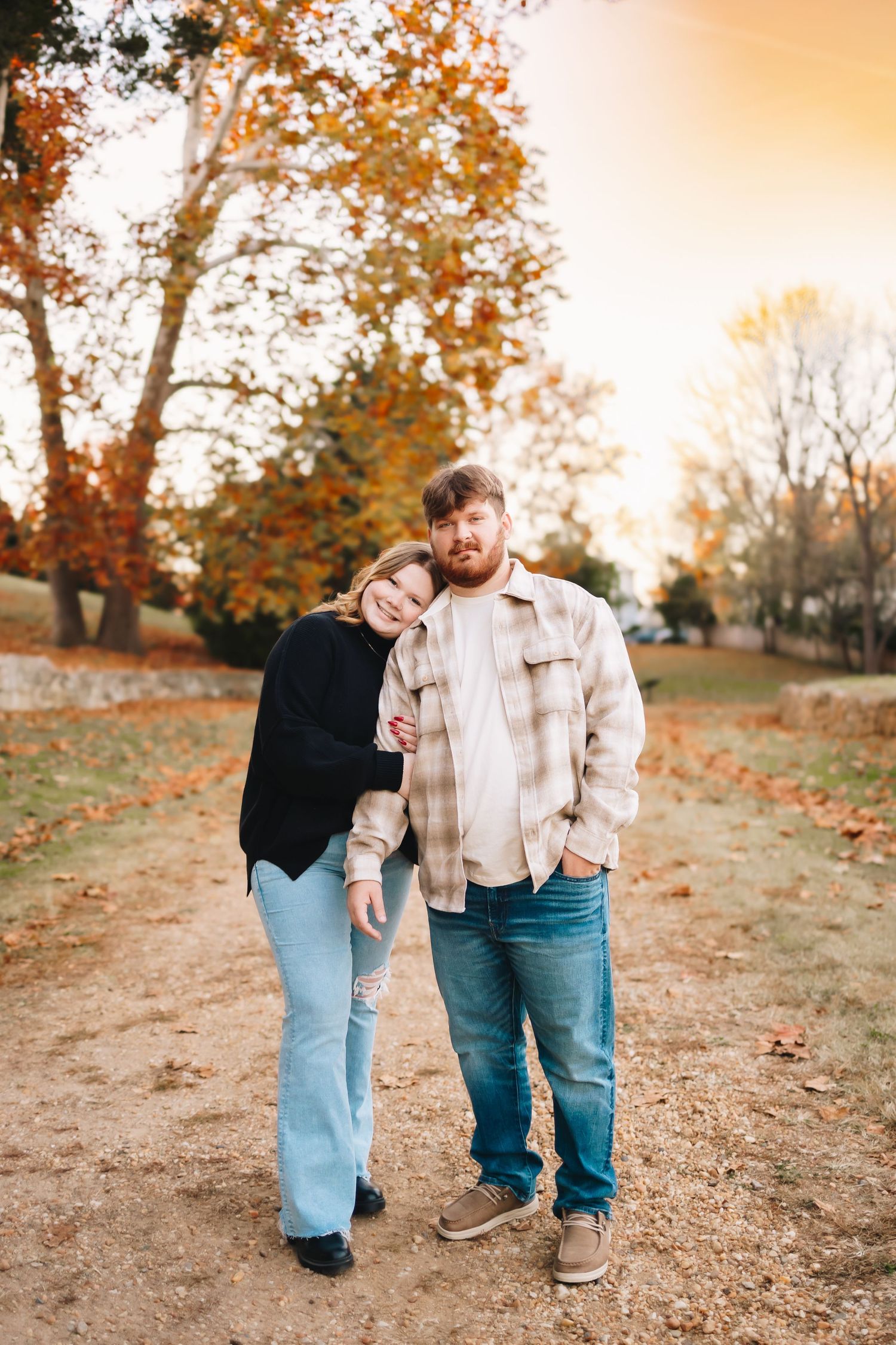 A couple walking together on a hill during autumn with golden leaves scattered on the ground.