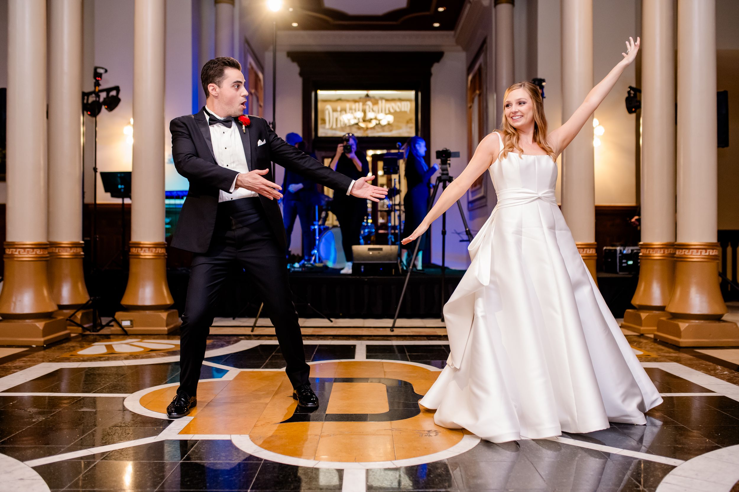 A wedding couple shares a fun light saber duel on their reception dance floor while wearing formal attire.