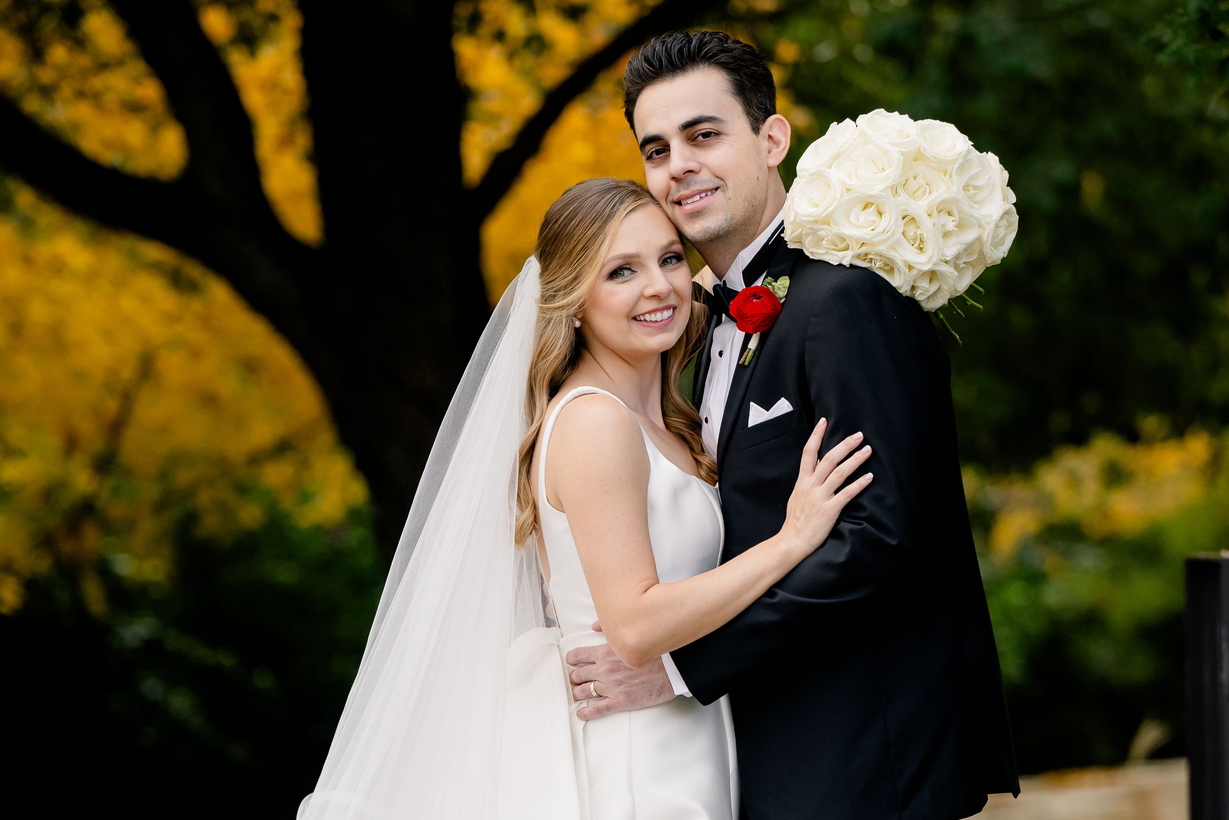A couple share an intimate moment on their wedding day with autumn yellow foliage in background.