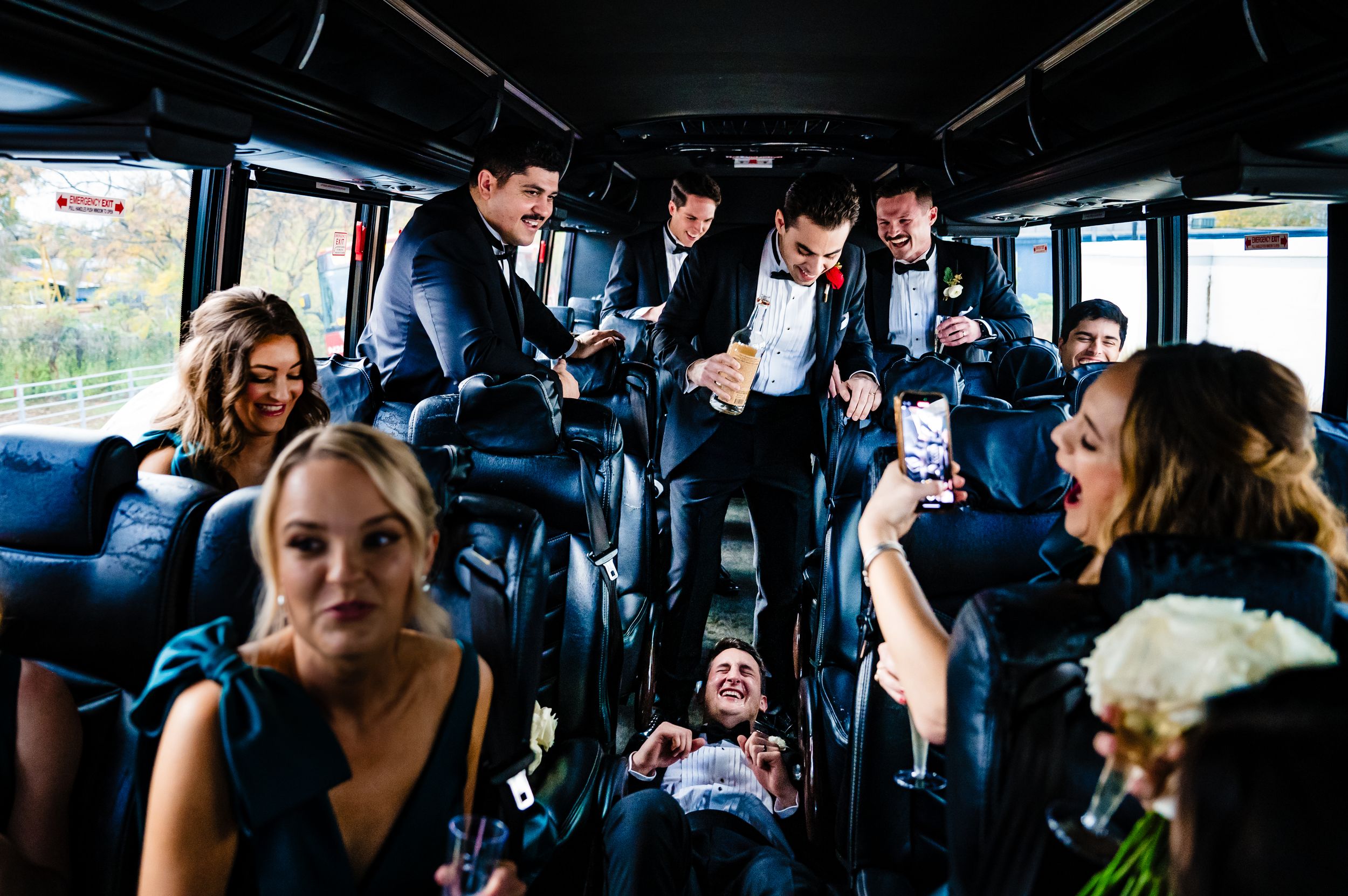 Wedding party members riding together on a bus, sharing drinks and conversation during a celebration.