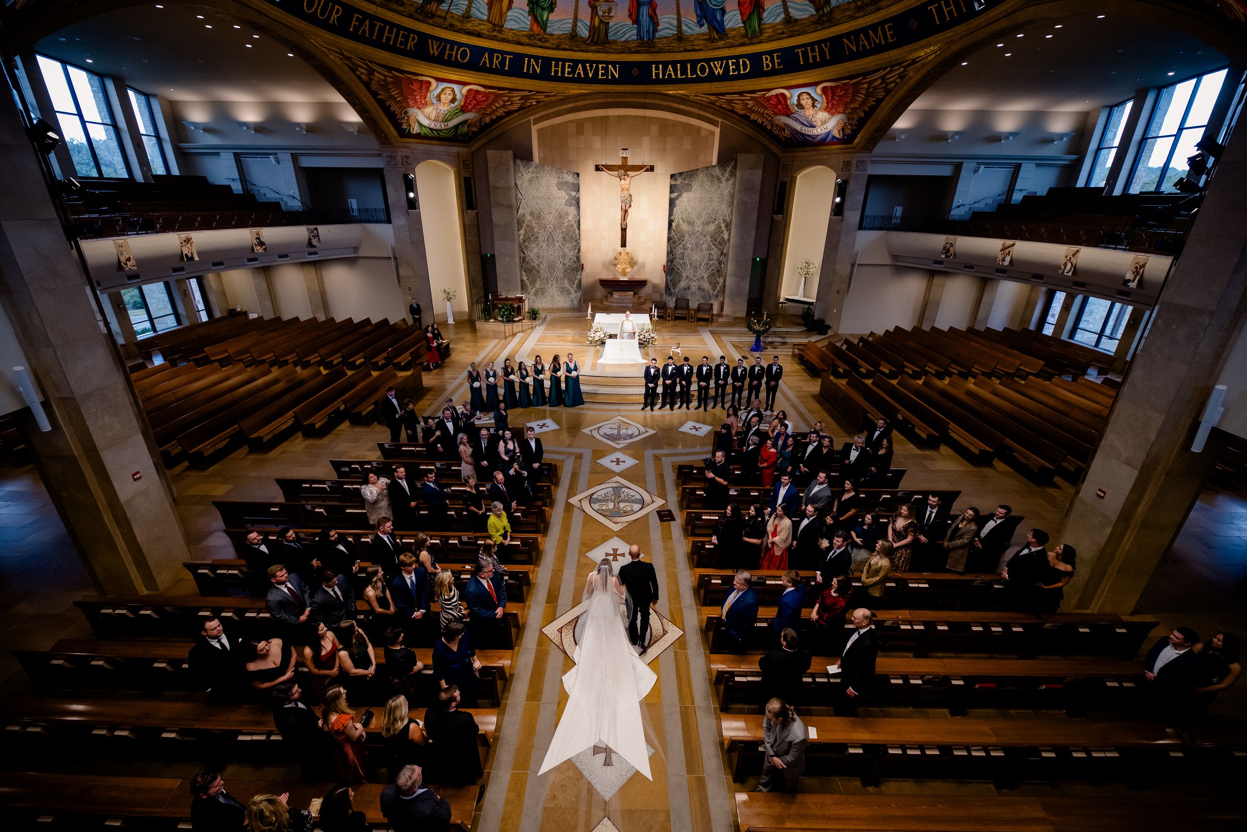 Aerial view of a traditional church wedding ceremony with guests seated in wooden pews and a long center aisle.