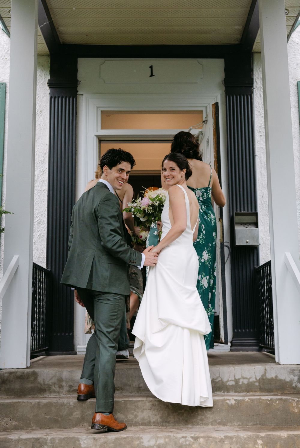 Happy couple shares a moment on concrete steps by decorative columns at a wedding entrance with number 1 above door.