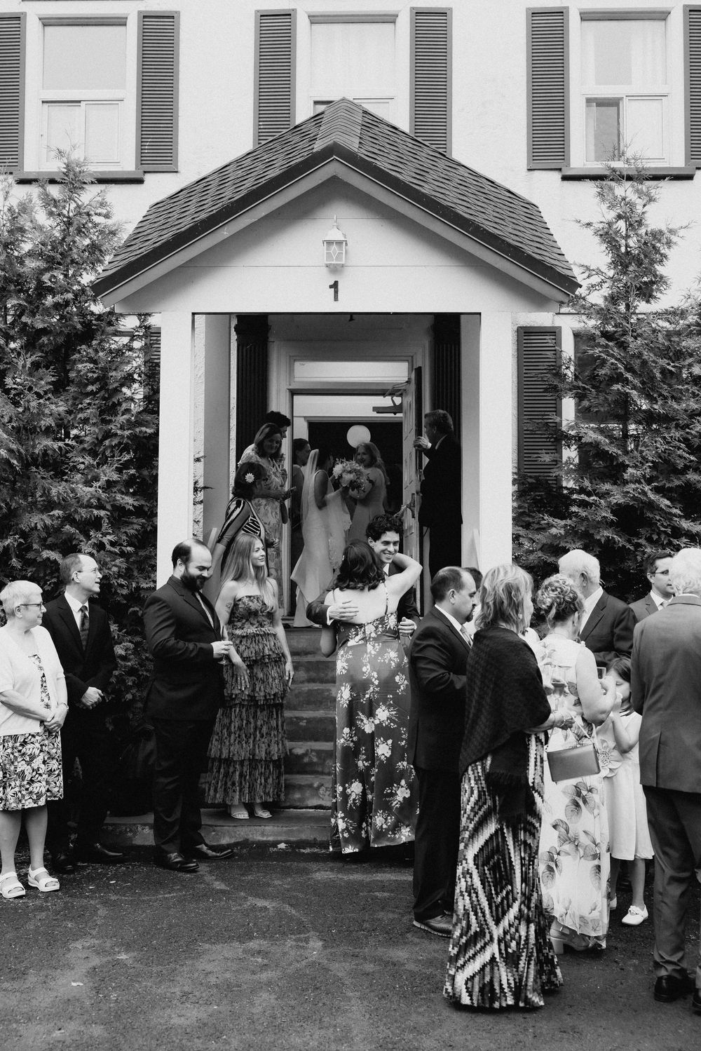 A group of people gather outside the entrance of a white house for a social event or gathering.