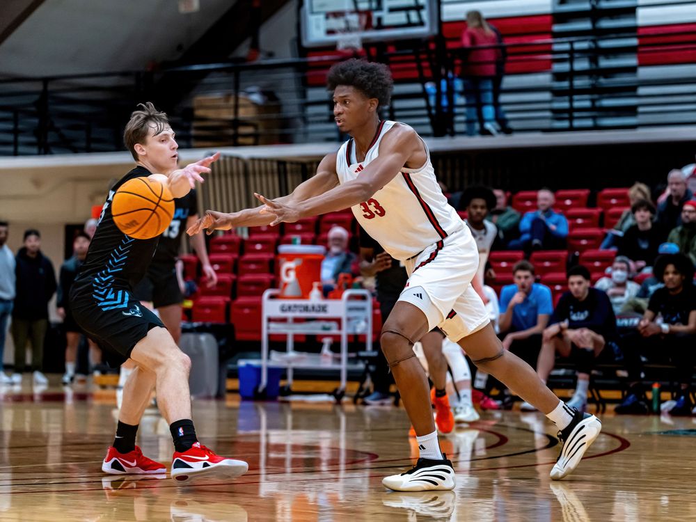 Two basketball players compete on an indoor court, one in white defending against an opponent in teal during a high school game.