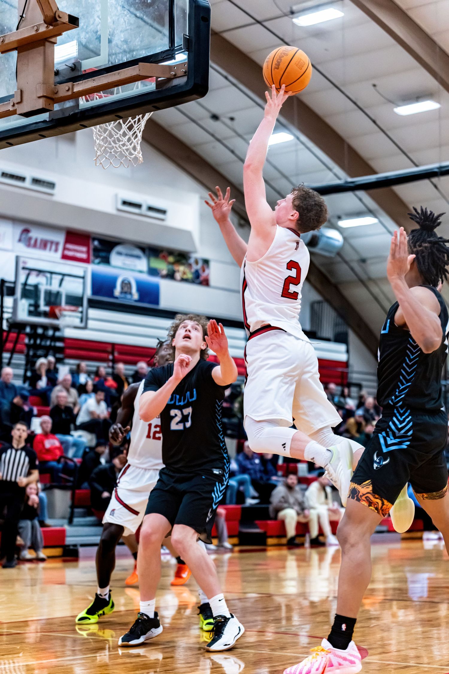 A basketball player in white jersey #2 leaps for a layup during an indoor high school basketball game.