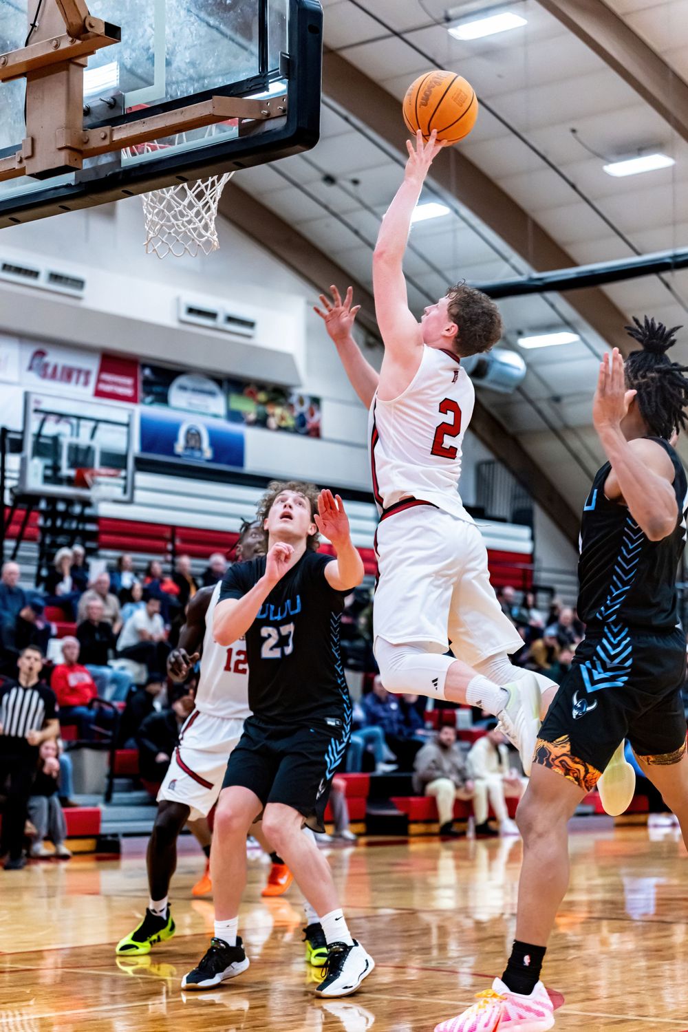 A basketball player in white jersey #2 leaps for a layup during an indoor high school basketball game.