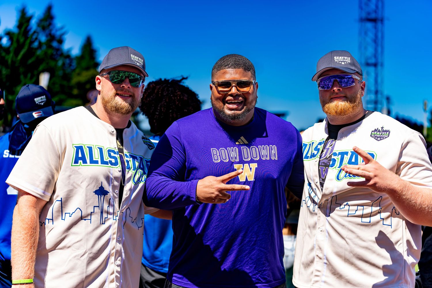 Three men pose together outdoors at an All-Star event, one wearing a purple Washington Huskies jersey.
