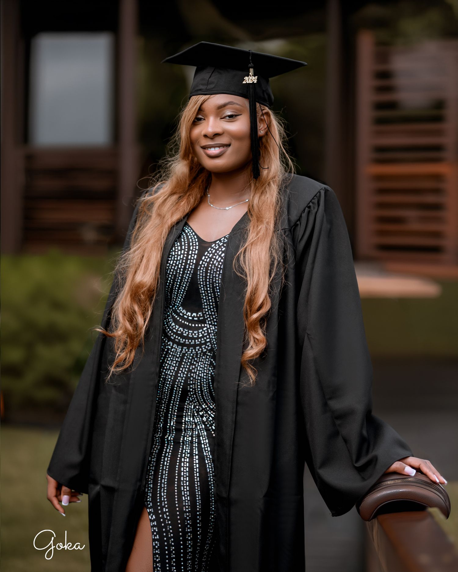 Graduate wearing black cap and gown with studded black dress poses during outdoor photoshoot ceremony celebration.