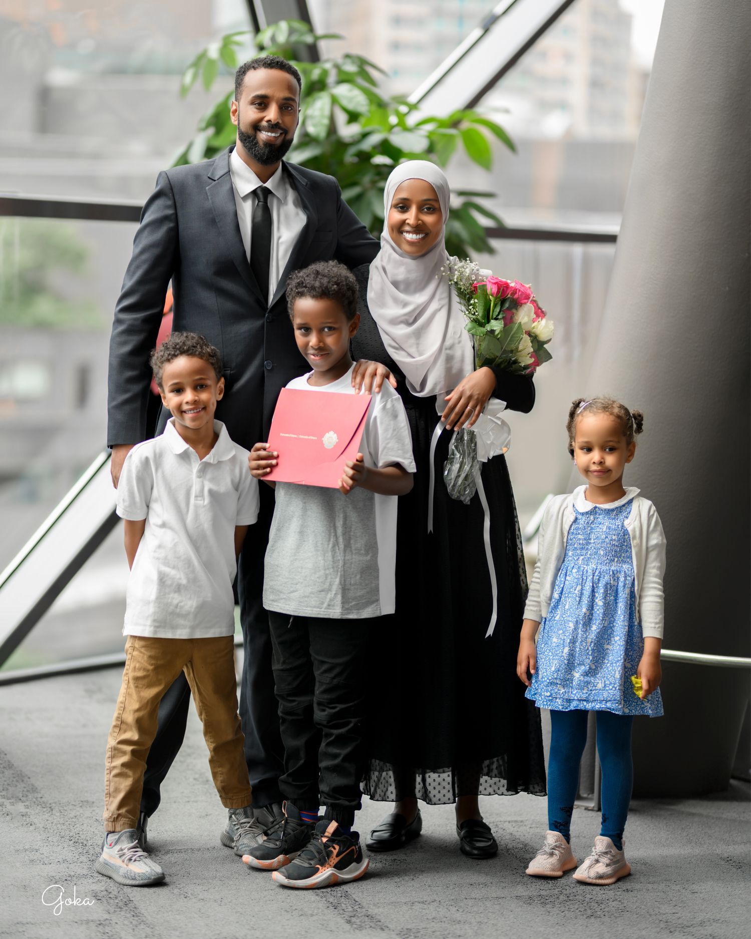 A family of five stands together in a bright indoor space holding graduation materials and flowers.