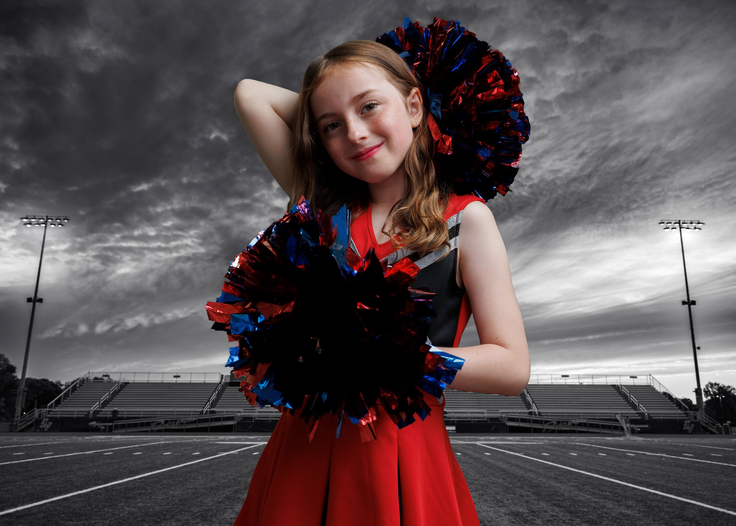 Cheerleader poses with pom poms on football field in selective color red against black and white background.
