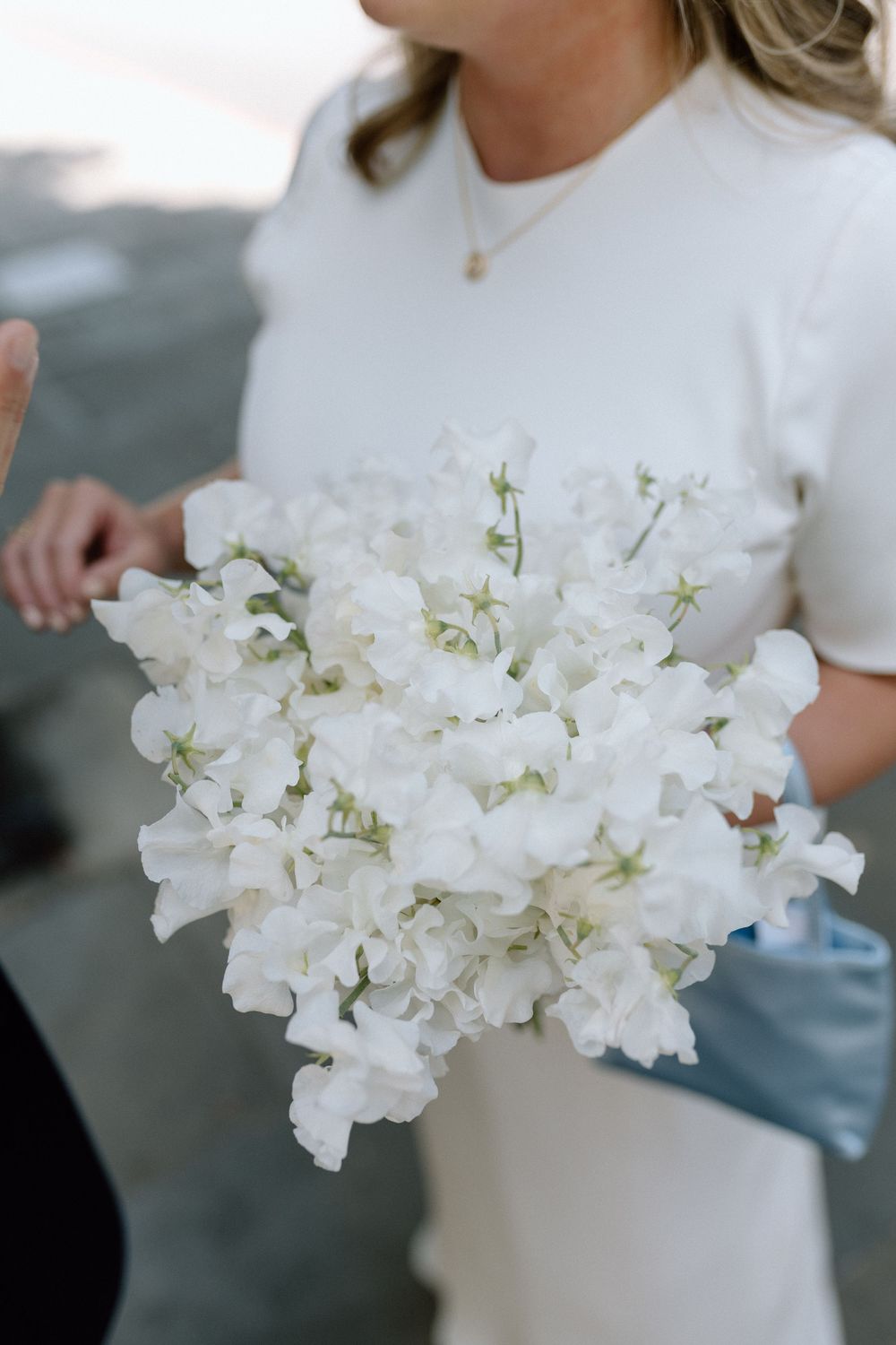 A delicate white sweet pea bouquet held against a white dress in soft natural lighting.