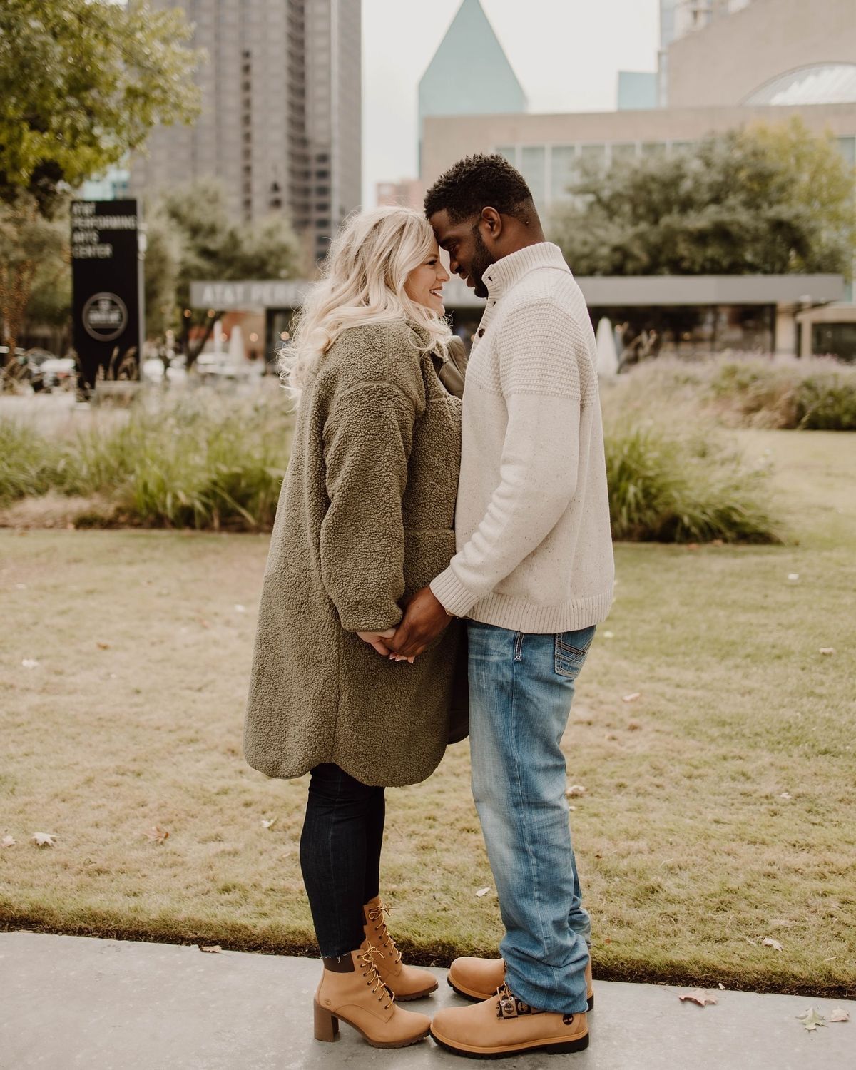 A romantic couple shares a tender moment while standing on a path in an urban park on an autumn day.