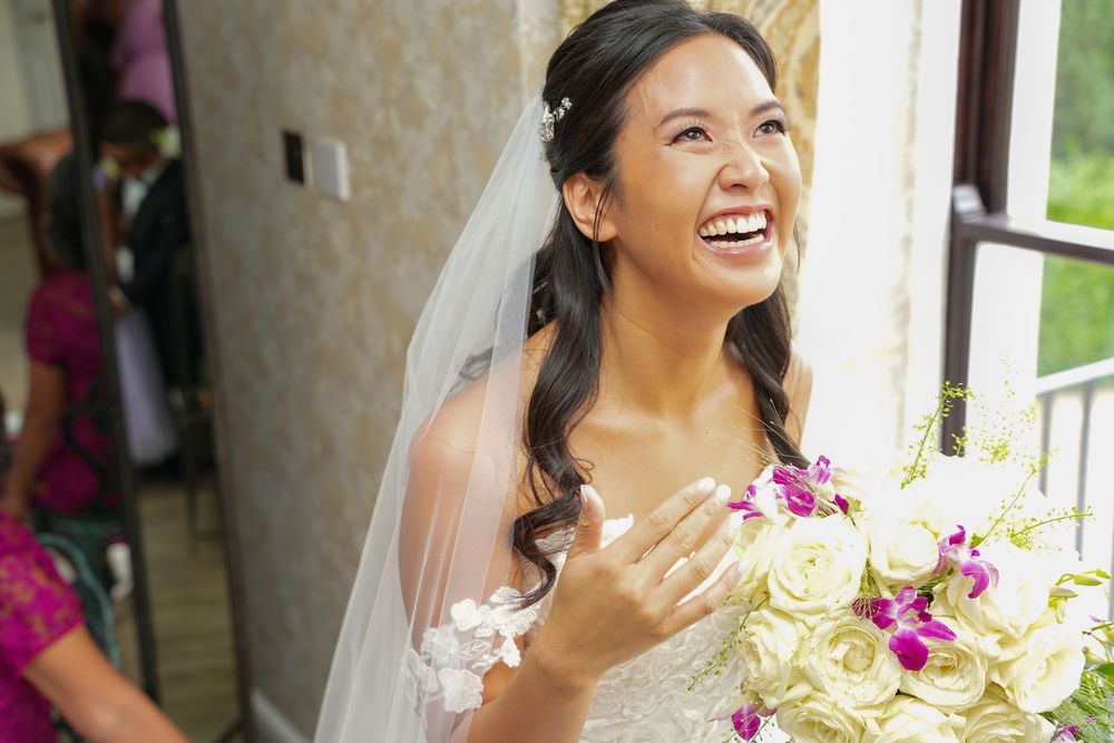 Joyful bride in white veil laughs while holding beautiful bouquet of white roses and pink orchids.